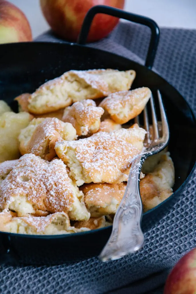 Nahaufnahme im 45-Grad-Winkel: Protein-Kaiserschmarrn bestreut mit Puder-Erythrit in einer schwarzen Servierpfanne