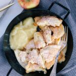 Protein-Kaiserschmarrn mit Apfelmus in einer schwarzen Servierpfanne auf einem dunkelblauen Leinentuch. Äpfel als Dekoration. Von oben fotografiert.