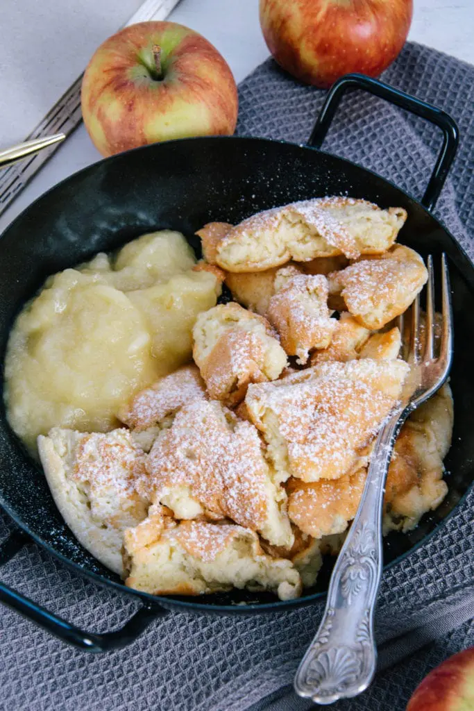 Protein-Kaiserschmarrn mit Apfelmus in einer schwarzen Servierpfanne auf einem grauen Leinentuch. Aufnahme im 45-Grad-Winkel.