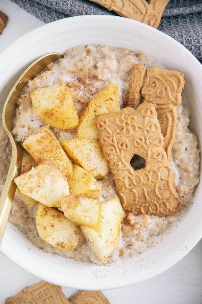 Spekulatius-Porridge mit Bratapfel in einer weißen Schüssel mit goldenem Löffel. Nahufnahme von oben.