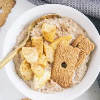 Spekulatius-Porridge mit Bratapfel in einer weißen Schüssel mit goldenem Löffel. Aufnahme von oben.