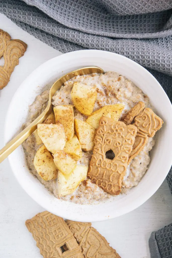 Spekulatius-Porridge mit Bratapfel in einer weißen Schüssel mit goldenem Löffel. Aufnahme von oben.