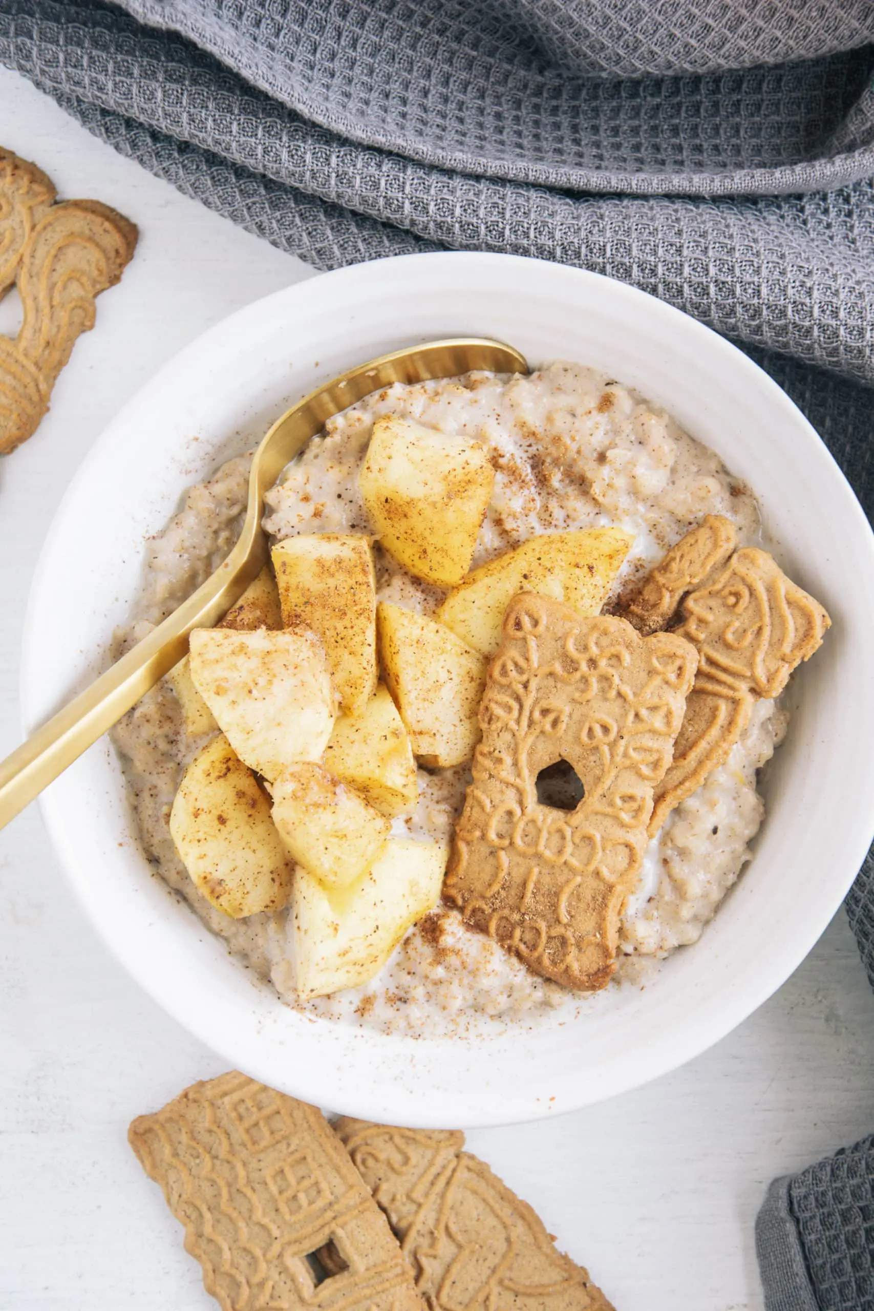 Spekulatius-Porridge mit Bratapfel in einer weißen Schüssel mit goldenem Löffel. Aufnahme von oben.
