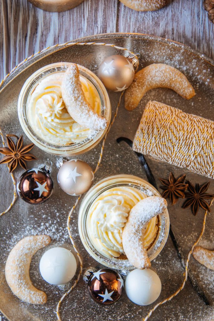 Vanillekipferl-Cheesecake-Dessert mit Mandelnougat auf einem goldenen Teller mit einer Rolle Glitzergarn als Dekoration. Aufnahme von oben.