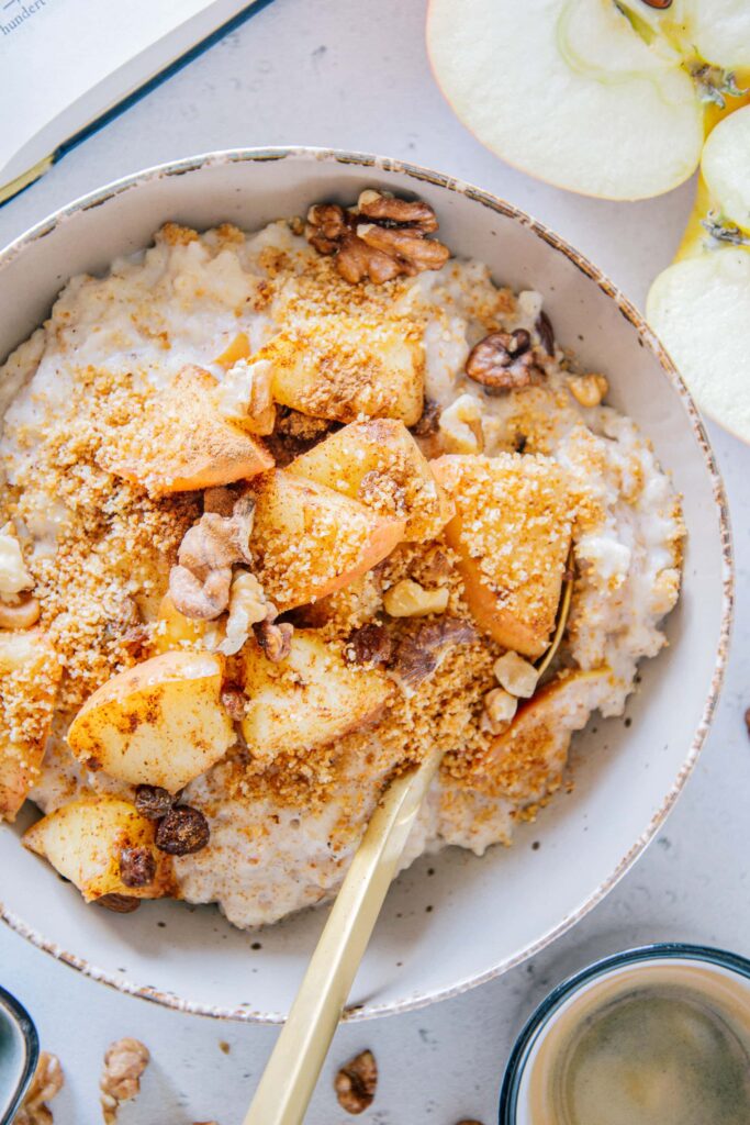 Nahaufnahme von Apfelstrudel-Porridge mit Rosinen und Knusperbröseln von oben in einer grauen Schüssel.