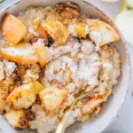 Mit einem goldenen Löffel durchgerührter Apfelstrudel-Porridge. Nahaufnahme von oben, sodass die cremige Konsistenz deutlich sichtbar ist.