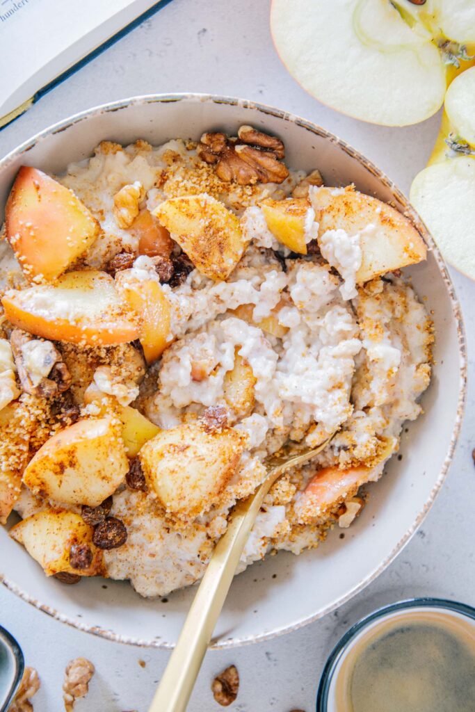 Mit einem goldenen Löffel durchgerührter Apfelstrudel-Porridge. Nahaufnahme von oben, sodass die cremige Konsistenz deutlich sichtbar ist.