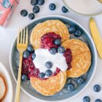 Gesunde glutenfreie Hafer-Chai-Pancakes mit Apfel-Beerenmus und Vanillejoghurt von oben fotografiert auf einem blauen Teller mit einer goldenen Gabel.