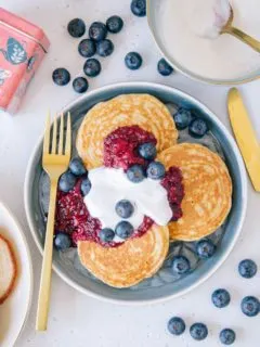 Gesunde glutenfreie Hafer-Chai-Pancakes mit Apfel-Beerenmus und Vanillejoghurt von oben fotografiert auf einem blauen Teller mit einer goldenen Gabel.