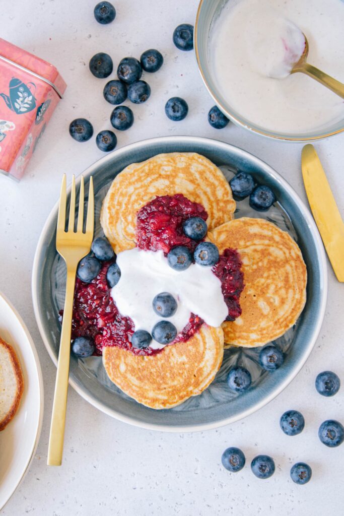 Gesunde glutenfreie Hafer-Chai-Pancakes mit Apfel-Beerenmus und Vanillejoghurt von oben fotografiert auf einem blauen Teller mit einer goldenen Gabel.