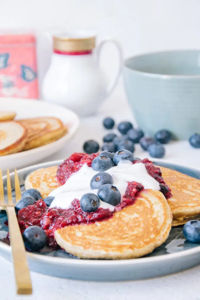 Gesunde glutenfreie Hafer-Chai-Pancakes aus der Nähe auf Augenhöhe fotografiert, mit Fokus auf dem Topping aus Apfel-Beerenmus, Vanillejoghurt und Heidelbeeren.