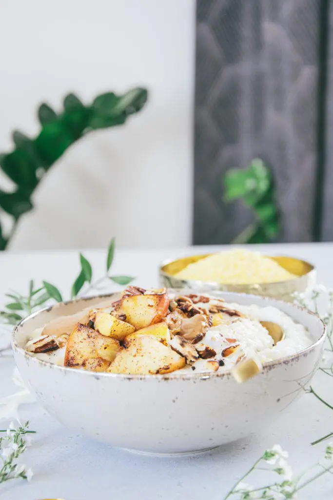 Hirse-Porridge mit Bratapfel in einer grauen Schüssel auf Augenhöhe fotografiert. Der goldene Löffel im Porridge lädt zum Essen ein.
