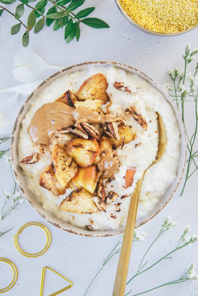 Eine Schüssel Hirse-Porridge mit Bratapfel von oben fotografiert auf hellem Untergrund. Topping aus Bratapfel, Mandelmus und gerösteten Pekannüssen.