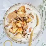 Eine Schüssel Hirse-Porridge mit Bratapfel von oben fotografiert auf hellem Untergrund. Topping aus Bratapfel, Mandelmus und gerösteten Pekannüssen.