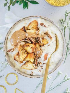 Eine Schüssel Hirse-Porridge mit Bratapfel von oben fotografiert auf hellem Untergrund. Topping aus Bratapfel, Mandelmus und gerösteten Pekannüssen.