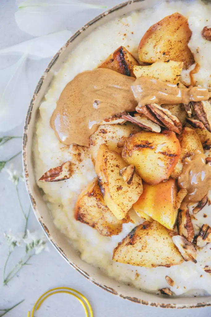 Nahaufnahme von Hirse-Porridge mit Bratapfel von oben. Schüssel von rechts angeschnitten. Details von Bratapfel und Mandelmus sind deutlich erkennbar.