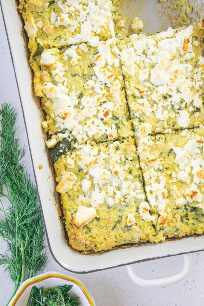 Hirse-Zucchini-Auflauf mit Dillsauce von oben fotografiert in einer alten weißen Emaille-Auflaufform. Auflaufform schräg oben rechts angeschnitten. Ein Stück Auflauf fehlt.