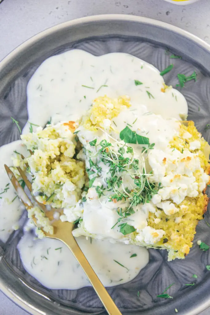 Nahaufnahme von einem Stück Hirse-Zucchini-Auflauf mit Dillsauce von oben mit einer goldenen Gabel.