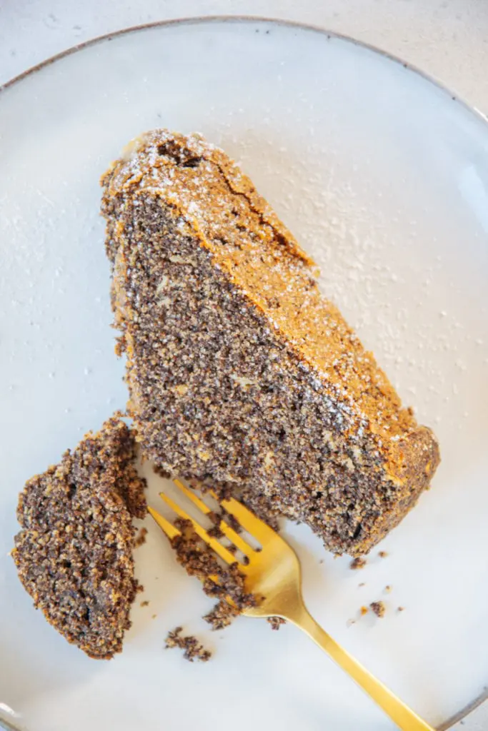 Ein Stück saftiger Low carb Mohnkuchen liegend von oben aus der Nähe fotografiert. Eine kleine goldene Gabel hat ein Stück Kuchen abgestochen.