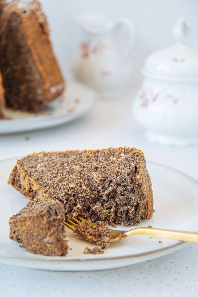 Ein Stück zuckerfreier Low carb Mohnkuchen auf Augenhöhe auf einem Teller, von einer goldenen Gabel angestochen, sodass die saftige Teigstruktur gut erkennbar ist.