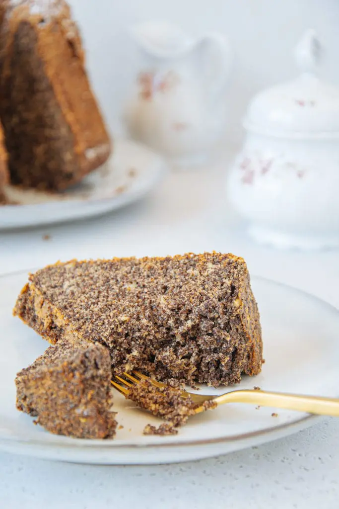 Ein Stück zuckerfreier Low carb Mohnkuchen auf Augenhöhe auf einem Teller, von einer goldenen Gabel angestochen, sodass die saftige Teigstruktur gut erkennbar ist.