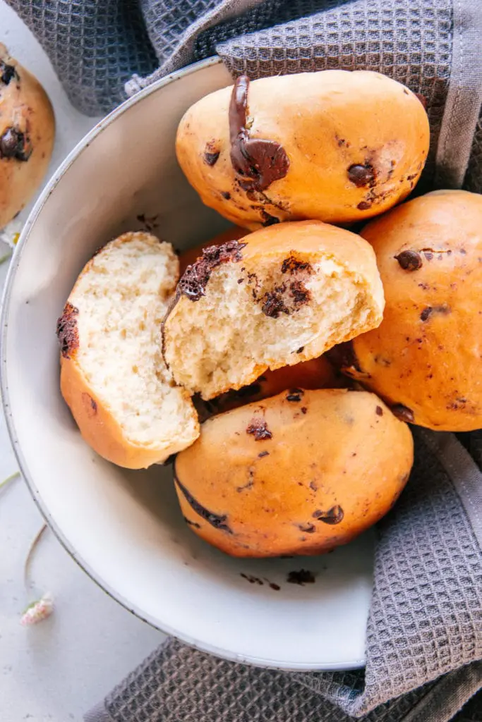 Schokobrötchen nach dem Grundrezept für veganen süßen Hefeteig ohne Zucker in einer großen Schüssel. Ein Brötchen ist in der Mitte auseinandergebrochen, sodass die feine, flaumige Teigstruktur sichtbar ist.