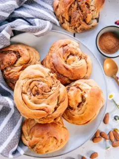 Mandel-Zimtknoten nach dem Grundrezept für veganen süßen Hefeteig ohne Zucker auf einem graublauen Teller mit einem grau-weißen Küchentuch als Dekoration.