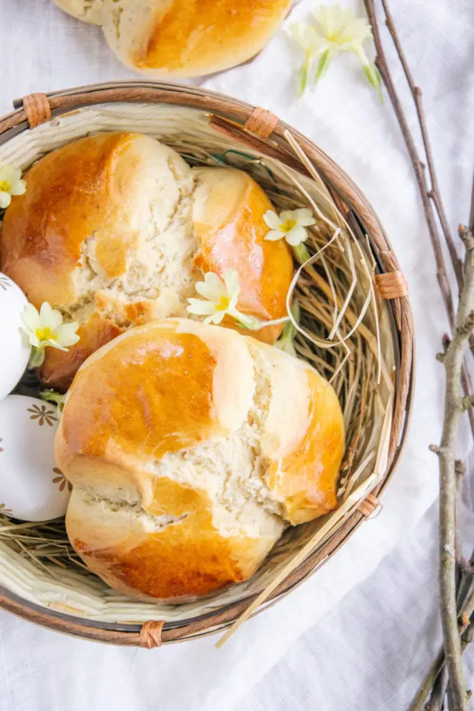 Zwei Dinkel-Osterpinzen ohne Zucker in einem geflochtenen Osternest. Mit Schlüsselblumen und Zweigen dekoriert.