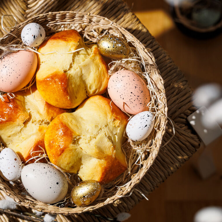 Drei Dinkel-Osterpinzen liegen in Osterkörbchen mit bunten Eiern und Ostergras.