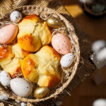 Drei Dinkel-Osterpinzen liegen in Osterkörbchen mit bunten Eiern und Ostergras.