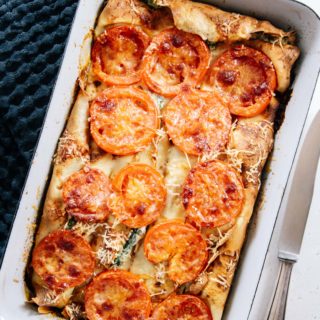 Ricotta-Spinat-Crespelle in einer weißen Emailleform diagonal im Bild stehend. Aufnahme von oben auf weißem Untergrund mit rustikalem Messer und schwarzem Wafflepick-Tuch