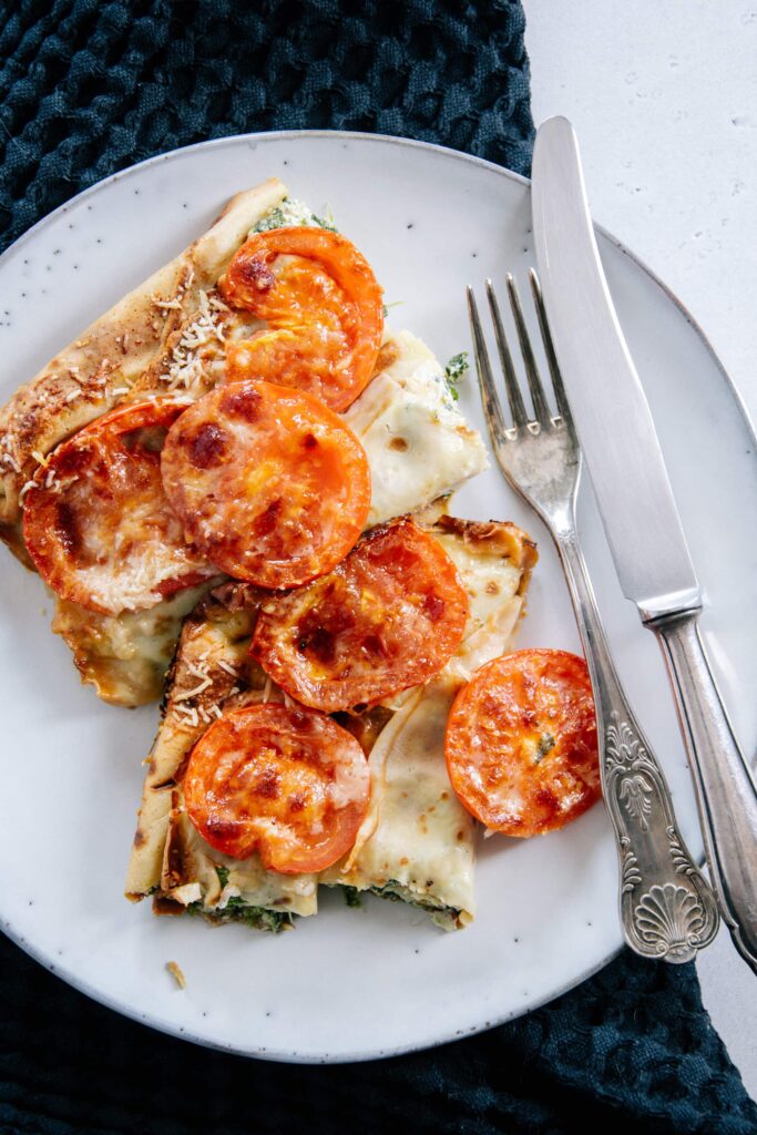 Überbackene Ricotta-Spinat-Crespelle auf einem graublauen Teller mit einer rustikalen silbernen Gabel. Aufnahme von oben.