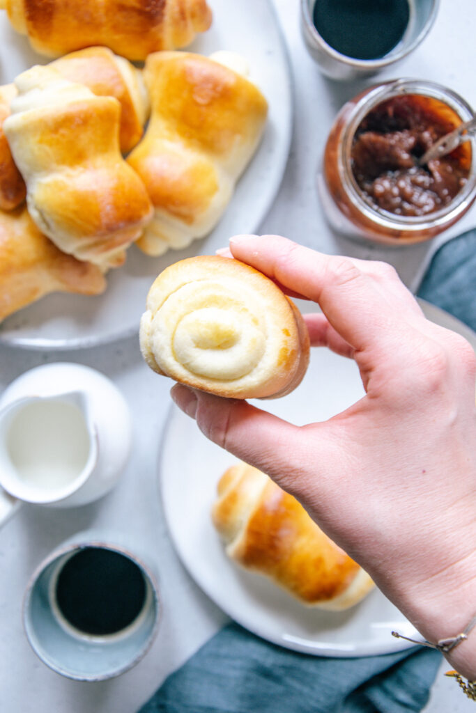 Eine Hand hält ein Milchbrötchen, sodass seitlich das spiralförmige Muster des aufgerollten Teiges sichtbar ist.