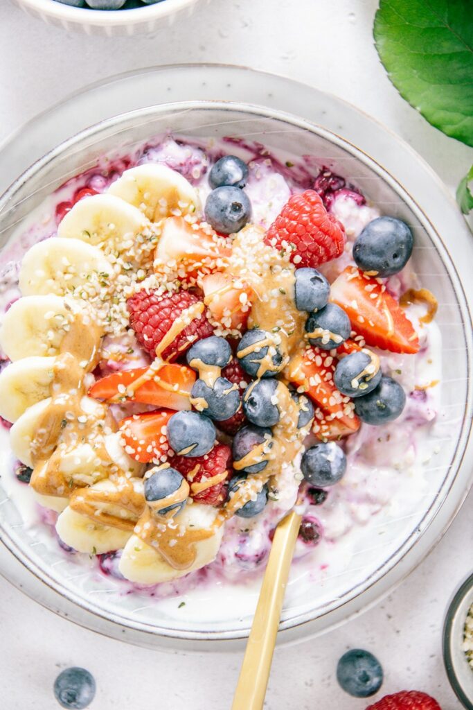 Nahaufnahme von Beeren-Bananen-Müsli von oben. Bananen, Beeren, Mandelmus und Hanfsamen als Topping.