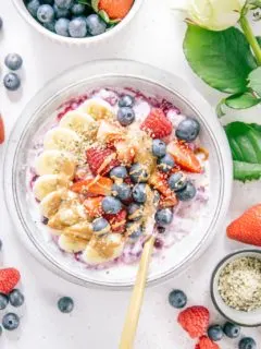 Schnelles Beeren-Bananen-Müsli mit Topping in einer graublauen Schüssel von oben fotografiert. Beeren und eine weiße Rose als Dekoration.