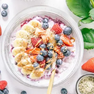 Schnelles Beeren-Bananen-Müsli mit Topping in einer graublauen Schüssel von oben fotografiert. Beeren und eine weiße Rose als Dekoration.