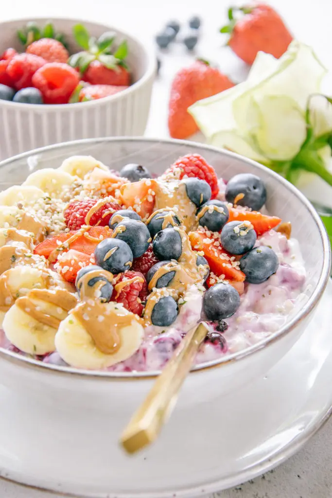 Schnelles Beeren-Bananen-Müsli in einer graublauen Müslischüssel mit goldenenm Löffel. Aufnahme im 45-Grad-Winkel.