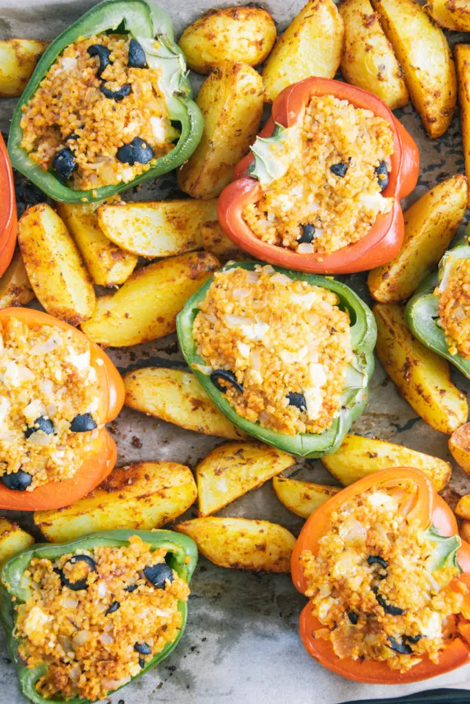 Gefüllte Bulgur-Feta-Paprika mit Ofen-Wedges von oben auf dem Backblech fotografiert. Bildfüllend ohne Deko.