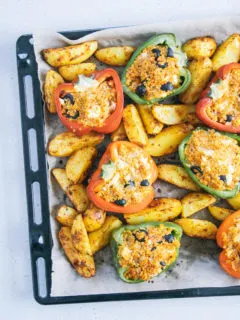 Gefüllte Bulgur-Feta-Paprika mit Ofen-Wedges auf dem Backblech von oben auf hellem Untergrund fotografiert. Blech auf der rechten Seite angeschnitten.