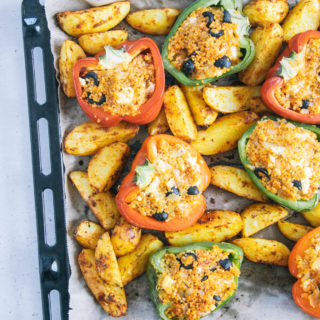 Gefüllte Bulgur-Feta-Paprika mit Ofen-Wedges auf dem Backblech von oben auf hellem Untergrund fotografiert. Blech auf der rechten Seite angeschnitten.