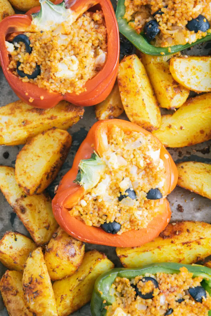 Nahaufnahme von Gefüllten Bulgur-Feta-Paprika mit Ofen-Wedges von oben. Details der Füllung und der Kartoffeln sind deutlich erkennbar.