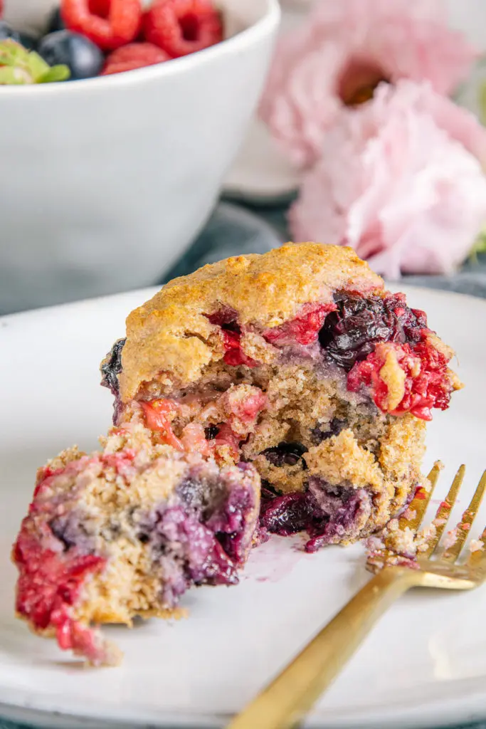 Ein veganer und zuckerfreier Beerenmuffin mit einer Gabel auseinandergestochen, sodass die weichen Beeren im inneren und die flaumige Textur des Teiges klar erkennbar sind.