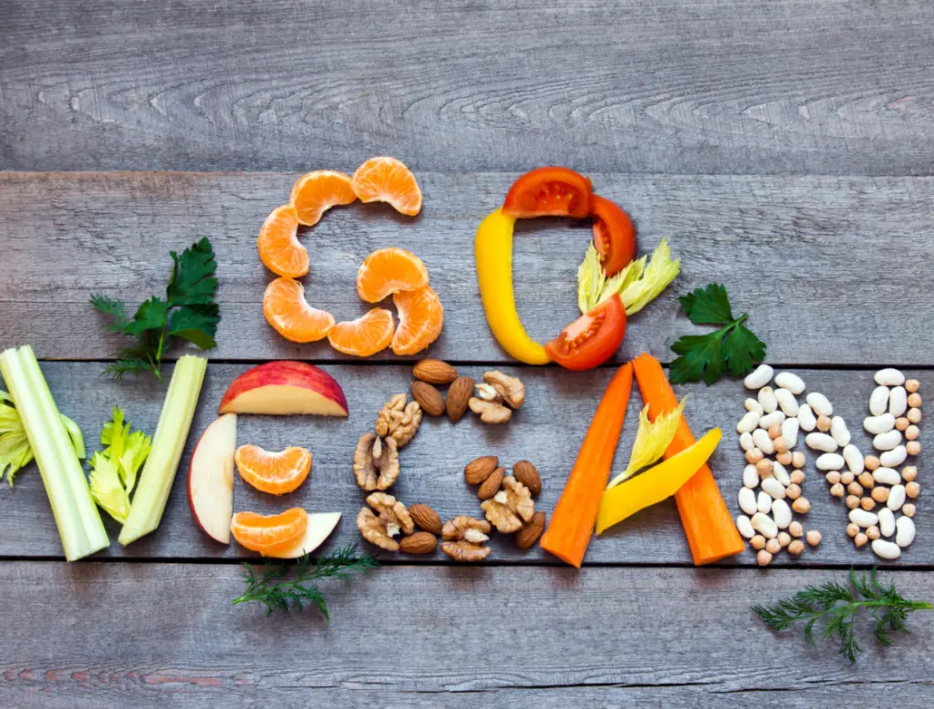 Die Worte "GO VEGAN" mit Gemüse und Obst auf einem Holzbrett geschrieben
