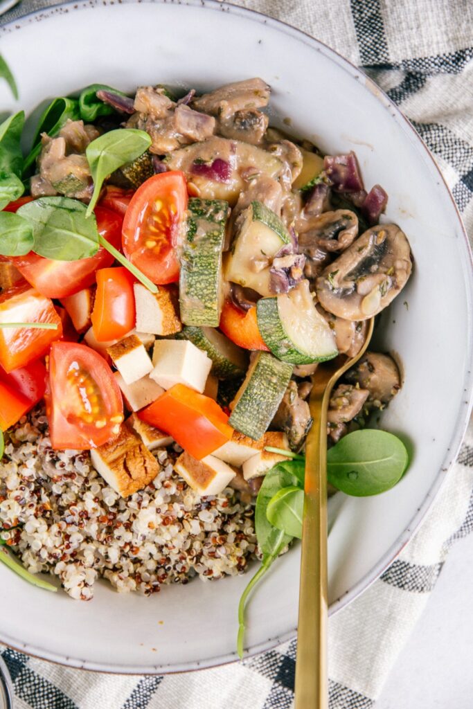 Nahaufnahme aus der Vogelperspektive von cremiger Pilzpfanne mit Zucchini, Räuchertofu, Tomaten und Quinoa.