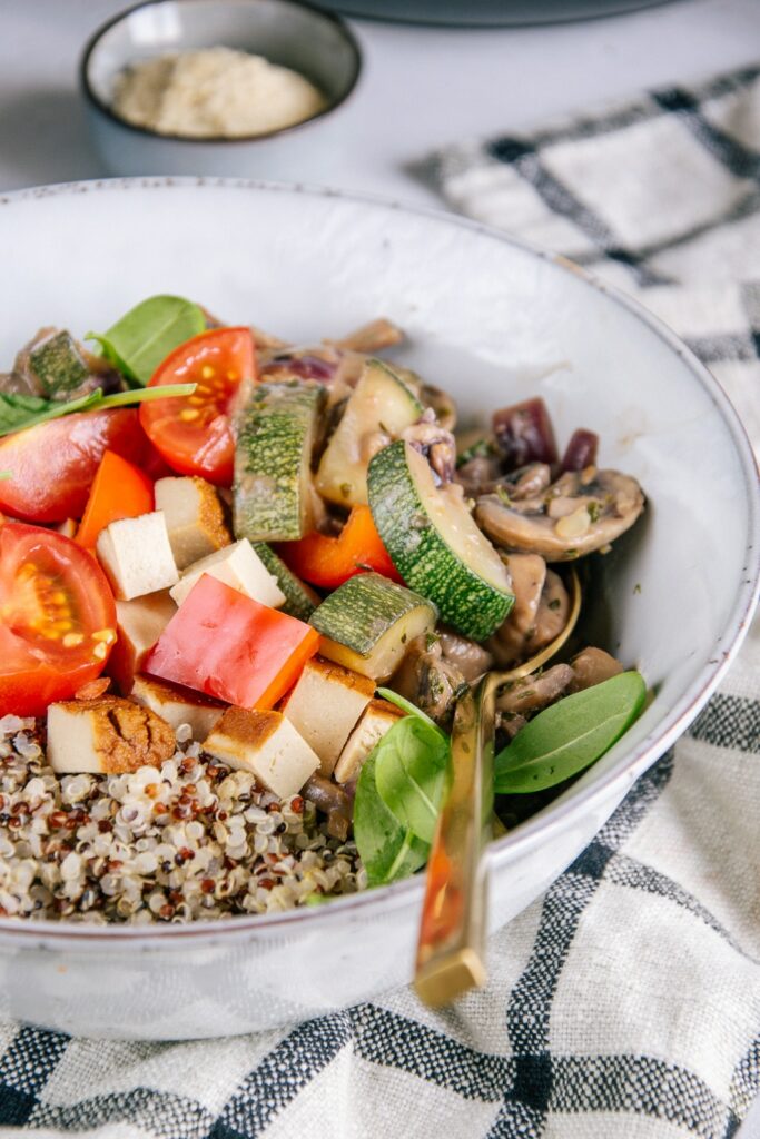 Quinoa, Räuchertofu, Tomaten und cremige Pilzpfanne in einer graublauen Schüssel. Nahaufnahme im 45-Grad-Winkel