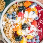 Nahaufnahme in Vogelperspektive von Porridge mit Nicecream. Topping aus Nektarinenstücken, gemischten Beeren, Kokoschips und Hanfsamen.