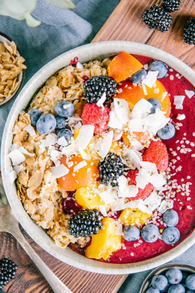 Nahaufnahme in Vogelperspektive von Porridge mit Nicecream. Topping aus Nektarinenstücken, gemischten Beeren, Kokoschips und Hanfsamen.