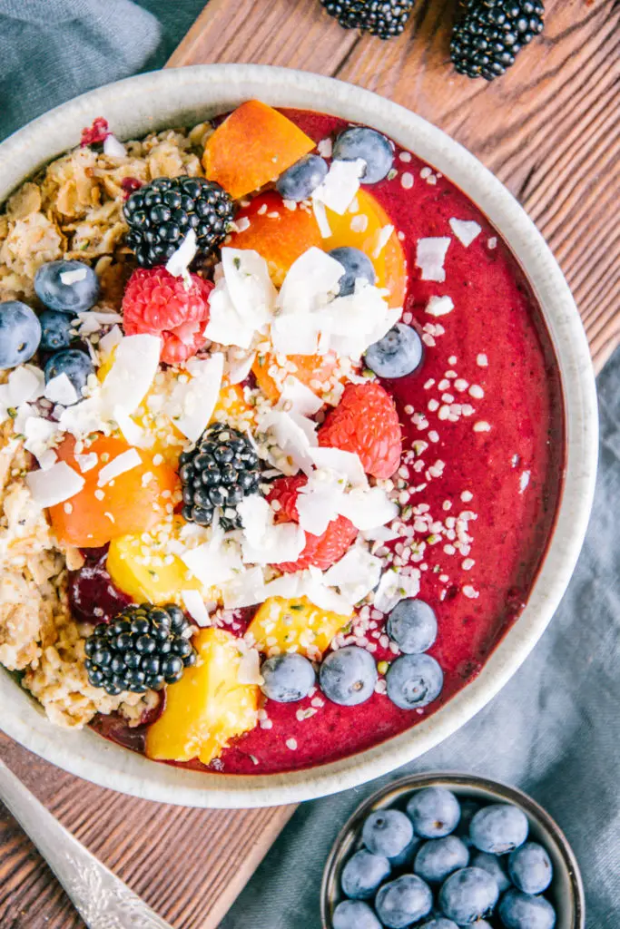 Porridge mit Nicecream in einer graublauen Schüssel aus der Vogelperspektive fotografiert. Schüssel links oben angeschnitten. Im Fokus die stark dunkelrosarote Nicecream mit den Details der Toppings.