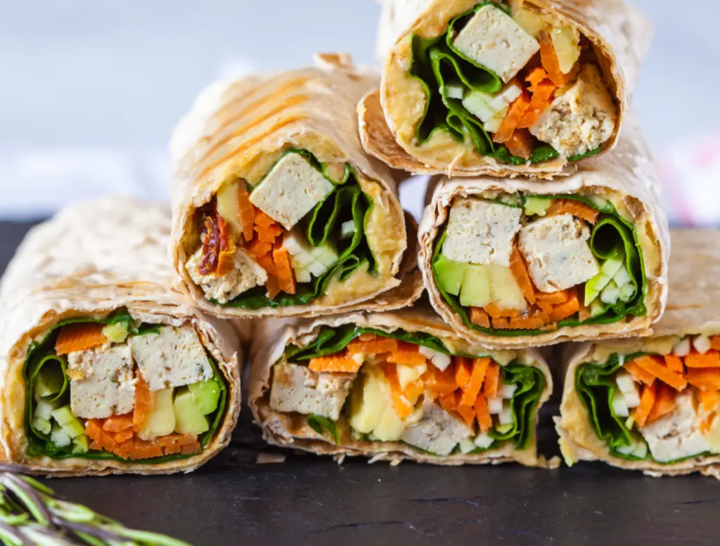 Vegan gefüllte Wraps auf Augenhöhe aufgenommen. Erfrischend aussehende Füllung mit Tofu, Avocado, Spinat, Hummus und Karotten.