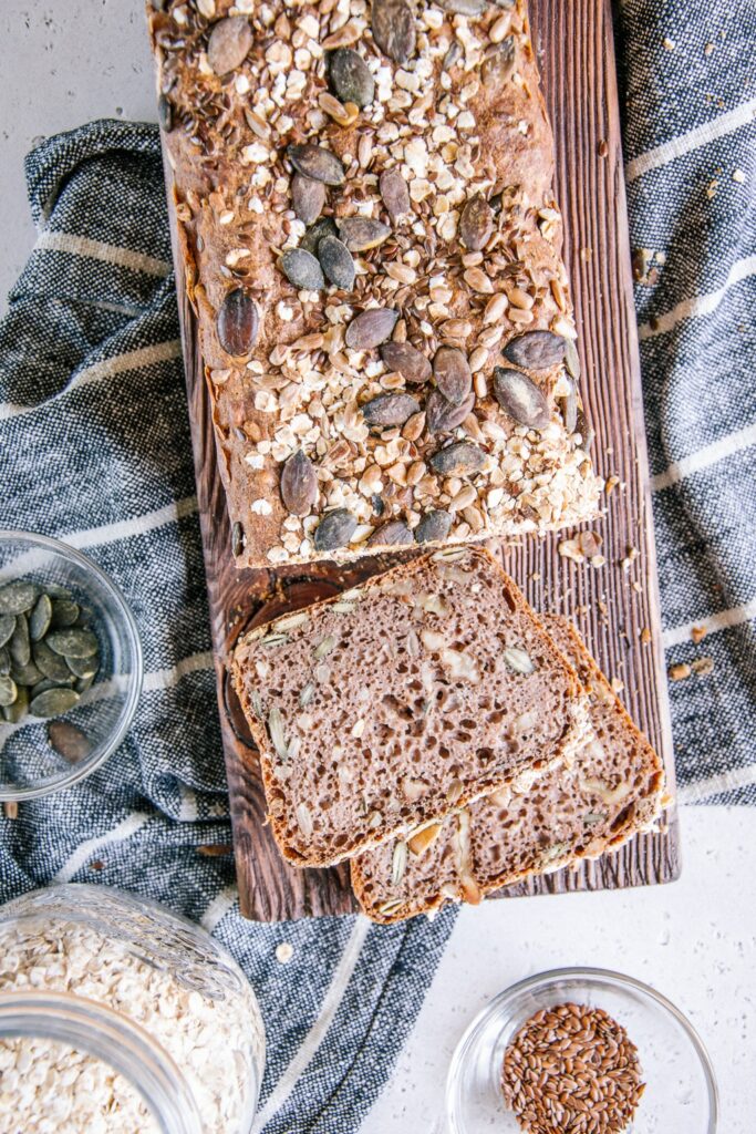 Angeschnittenes Vollkorn-Walnussbrot auf einem Holzbrett. Das Brot ragt von oben ins Bild und zwei Scheiben liegen bereits abgeschnitten daneben.